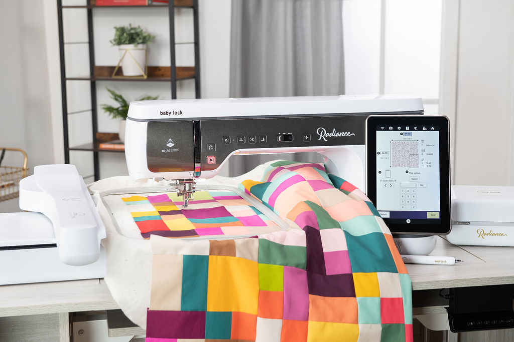 Baby Lock Radiance embroidery machine stitching a colorful geometric patchwork design, with a vibrant quilt draped over the worktable.