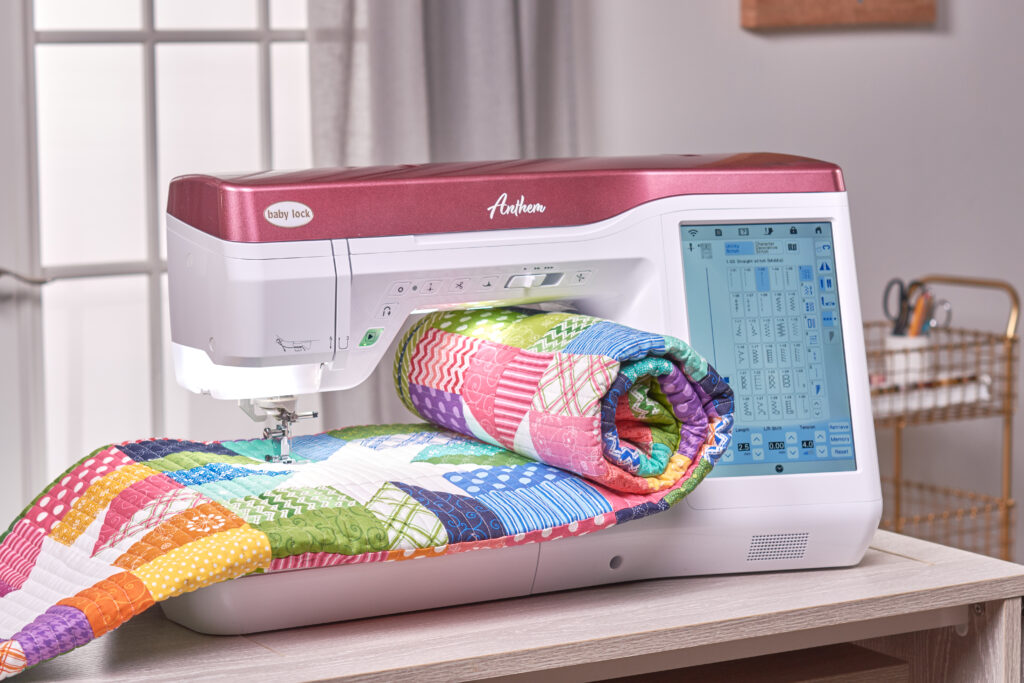 Baby Lock Anthem sewing machine with a colorful folded patchwork quilt extending through its sewing workspace.