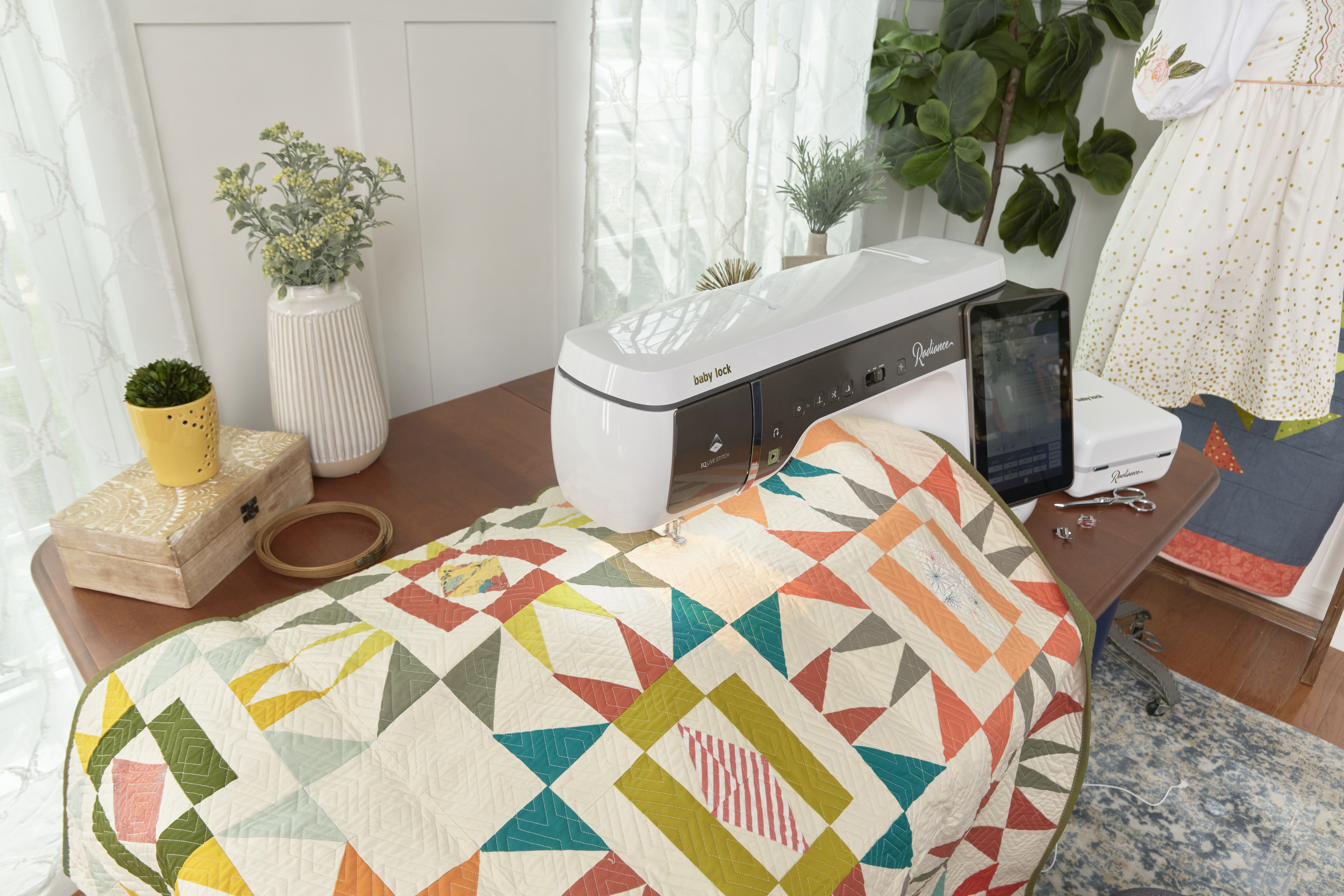 Baby Lock Radiance sewing and embroidery machine behind a geometric quilt in coral, peach, cream, olive and teal.
