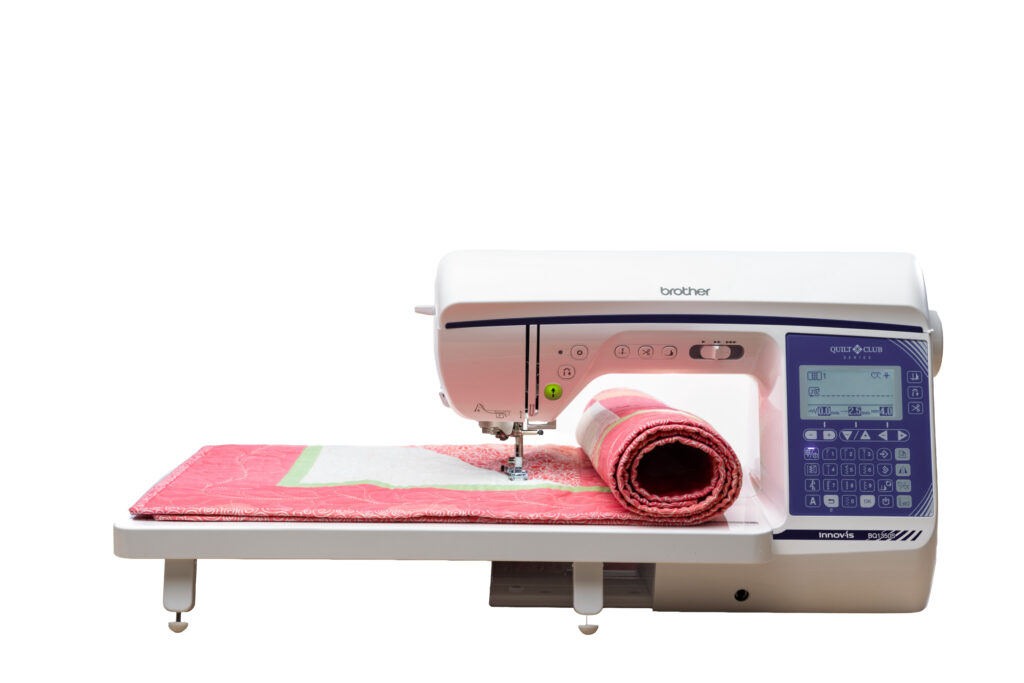 Brother Quilt Club BQ1350S sewing and quilting machine stitching a pink quilt with fabric rolled through the workspace.
